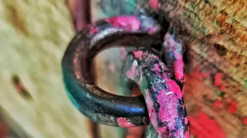 Rusty chain with pink paint on wood wall.