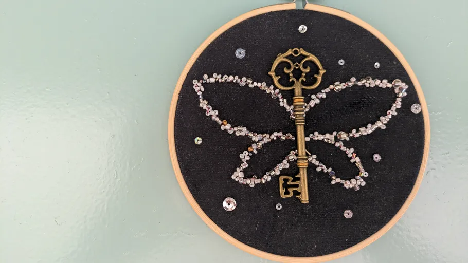 Key and beads forming butterfly on fabric.