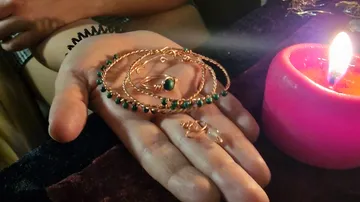 Hand holding jewelry near lit candle.