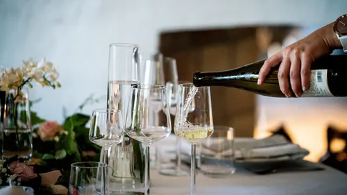 Hand pouring wine into glasses, elegant setting.