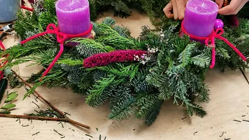 Fertiger Adventskranz mit weißen Kerzen, Zapfen und roten sowie weißen Kugeln.