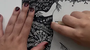 Hands carving intricate black linocut design.