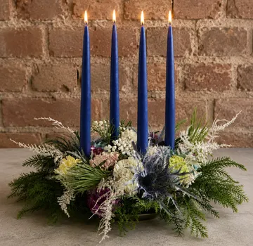 Blue candles in floral arrangement, brick background.
