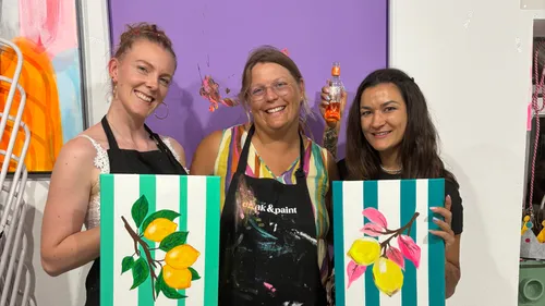 Three women displaying painted lemon artworks.