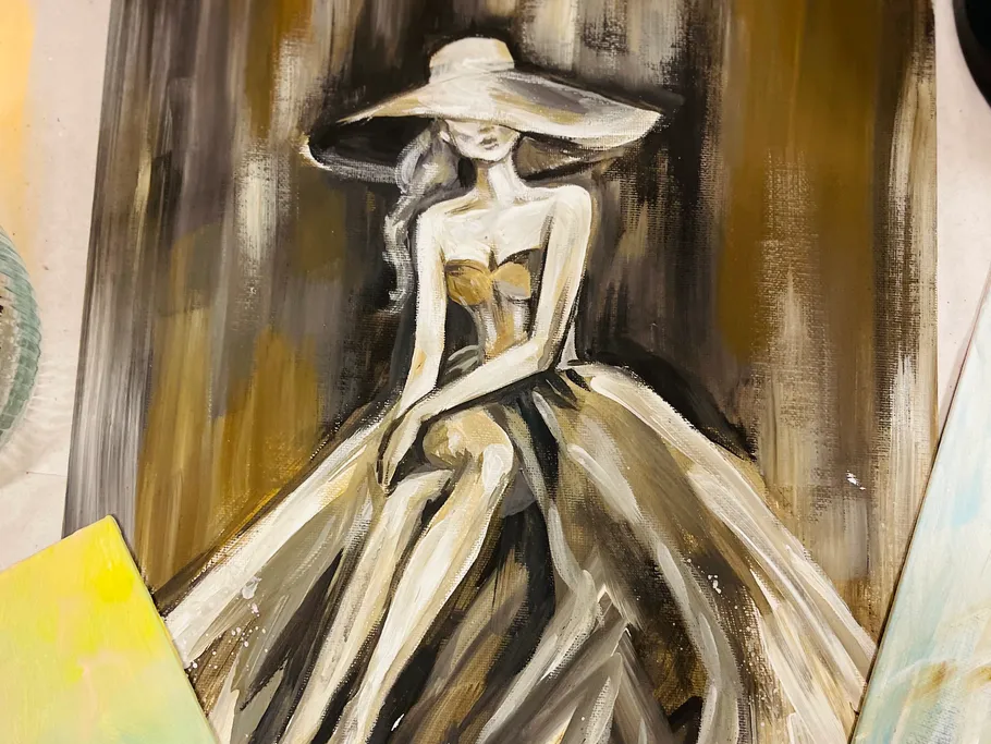 A woman wearing a hat is sitting in a painted dress.