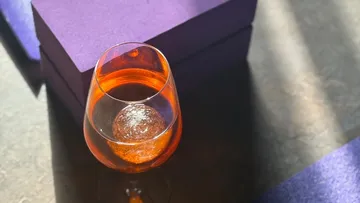 Glass of orange drink beside purple box.