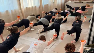 People in yoga pose holding drinks, indoors.