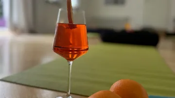Glas mit orangefarbenem Getränk auf grünem Teppich.