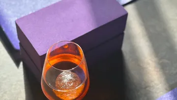 Glas mit Orangensaft neben lila Box.