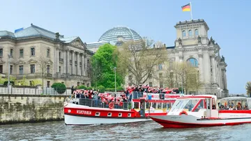 Touristenboote auf Fluss bei historischen Gebäuden.