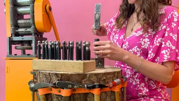 Woman hammering jewelry in colorful workspace.