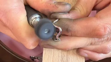 Hands polishing metal wire on wooden surface.