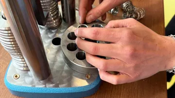 Hände justieren Metallgerät auf Holztisch.
