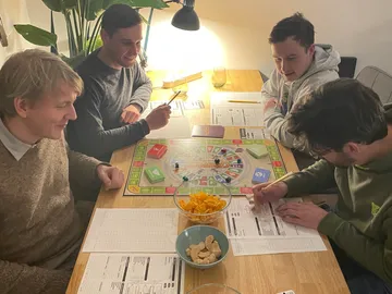 Vier Männer spielen ein Brettspiel, Snacks liegen bereit.
