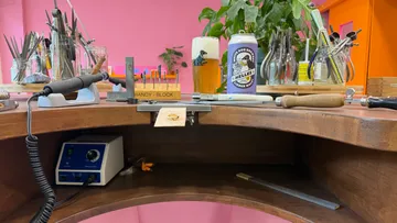 Jewelry workshop bench with tools and drink.