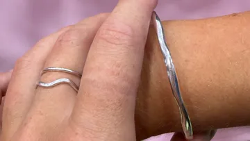 Hände tragen wellenförmigen Silberschmuck.