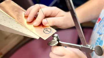 Hände schneiden Kupfer mit einer Laubsäge.