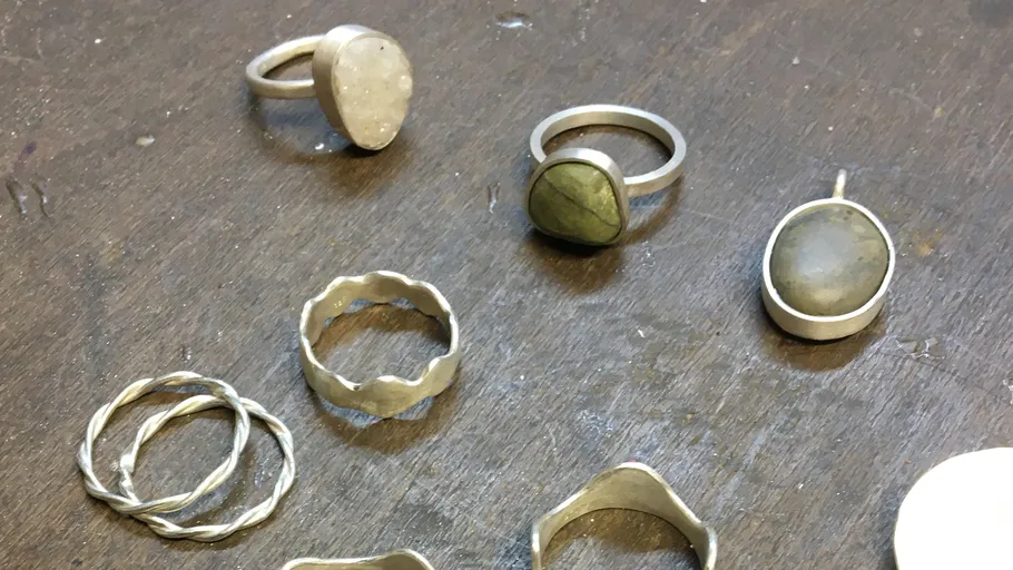 Silver rings and pendant on wooden surface.