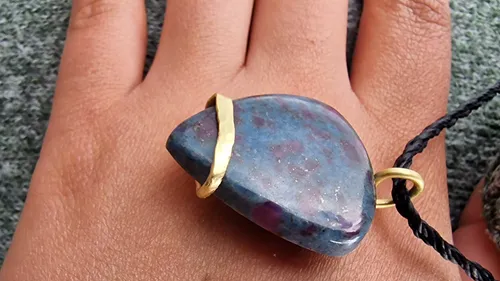 Hand wearing gemstone pendant, textured surface.