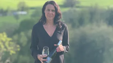 Frau hält Weinflasche und Glas im Freien.