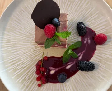 Dessert mit Schokolade, Beeren, Minzblättern auf Teller.