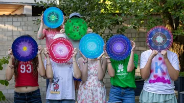 Kinder halten bemalte Scheiben vor Gesichter im Freien.