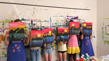 Children holding colorful paintings in art studio.