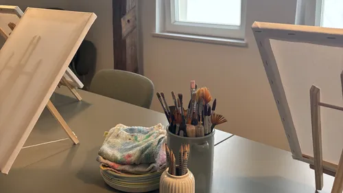 Paintbrushes in jar on table by canvases.