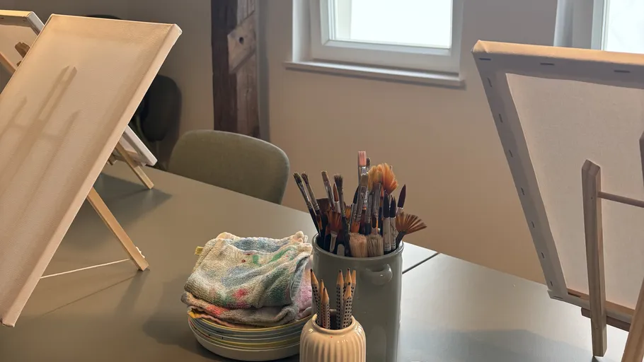 Paintbrushes in jar on table by canvases.