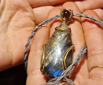 Hand holding decorative gemstone pendant indoors.