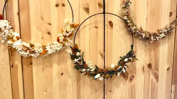 Three floral wreaths hanging on wooden wall.