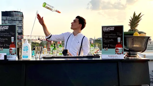 Bartender expertly tossing bottle on rooftop.