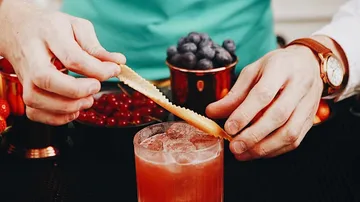 Hands garnish drink with citrus peel.