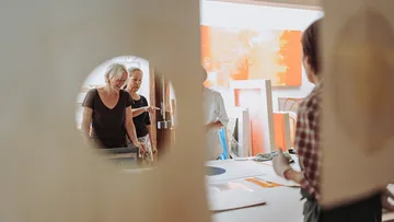 Frauen betrachten Kunstwerke in einem Atelier durch Türen.