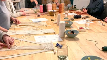 People crafting macramé at wooden table.