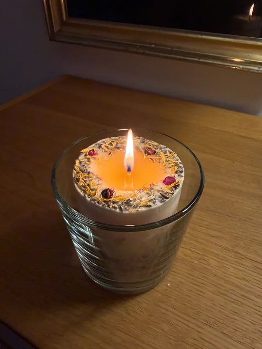 Kerze brennt in Glas auf Holztisch.