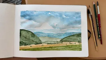 Aquarelllandschaft im Skizzenbuch mit Pinseln daneben.