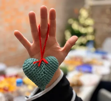Hand hält gehäkeltes Herzornament drinnen.