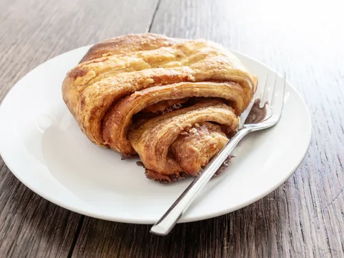 Yeast pastry is placed on a plate with a fork on a wooden surface.