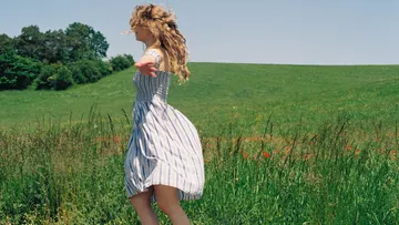 Woman spinning in grassy field under blue sky.