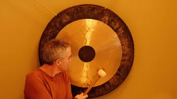 Person schlägt einen großen Gong drinnen.