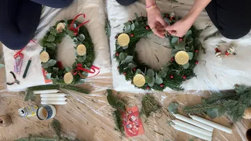 Zwei Hände schmücken Weihnachtskränze drinnen.