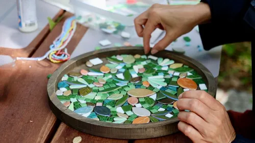 Hands arranging mosaic pieces on table.