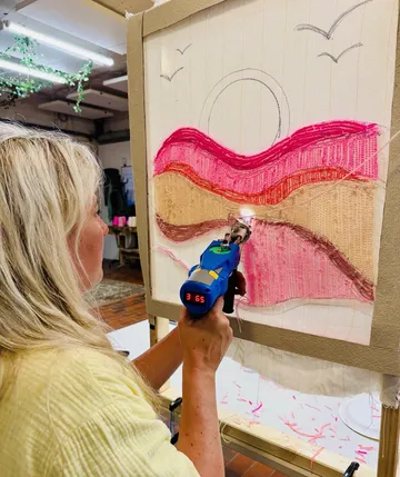 Person verwendet Tufting-Pistole auf Leinwandkunstwerk.
