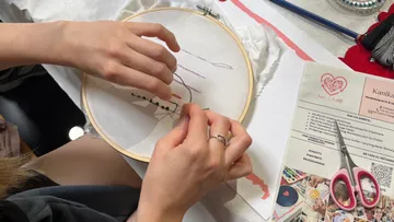 Hände sticken mit Stickrahmen auf Stoff.