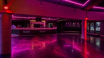 Leerer Nachtclub mit violetter Beleuchtung und Bar.