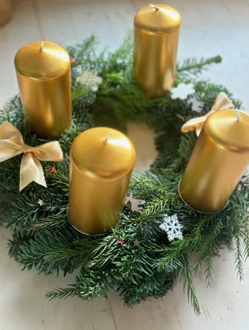 Goldene Kerzen auf grünem Weihnachtskranz.