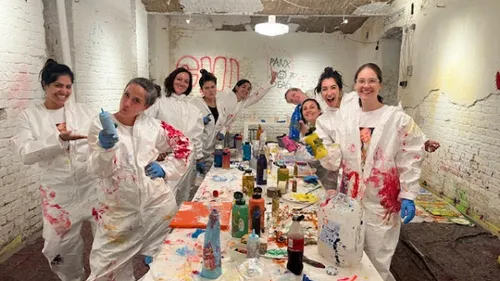People in paint-splattered suits in art studio.