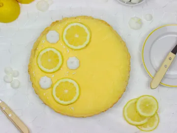 Lemon tart on a white table with lemon and silverware.