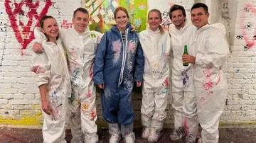 People wearing paint-splattered suits in art studio.